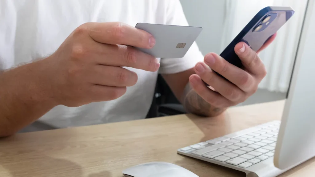 A person holding a payment card and smartphone while making an online transaction.