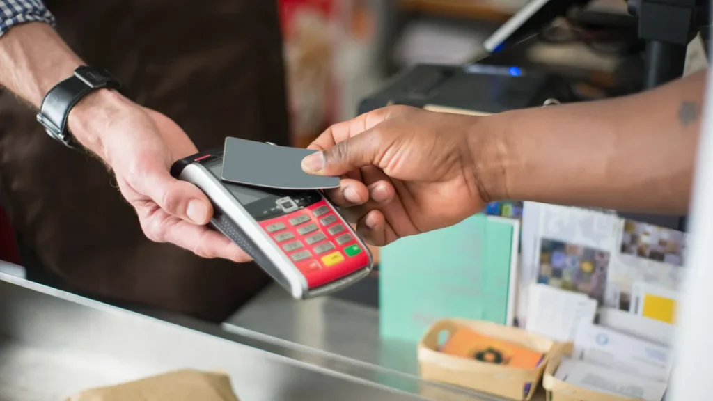 Customer holding a bank card to a contactless payment terminal at a retail checkout.