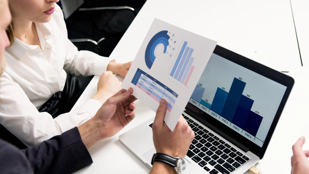 Business professionals reviewing printed charts beside a laptop displaying a bar graph.