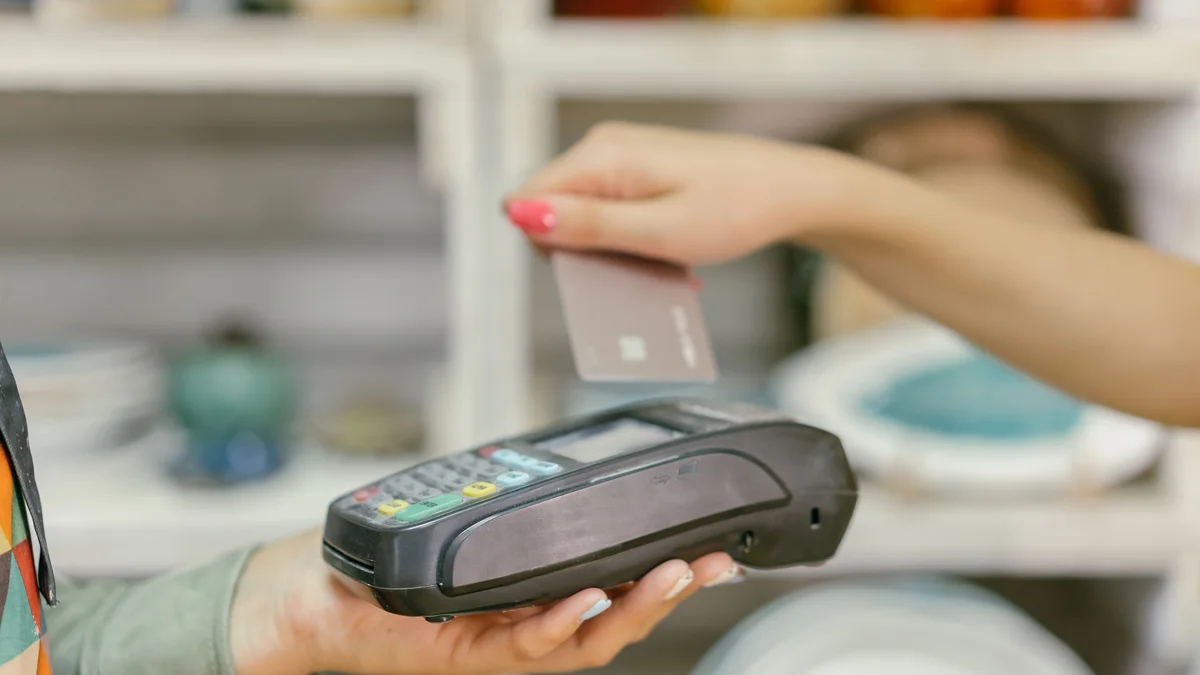 A customer holding a payment card over a point-of-sale terminal.
