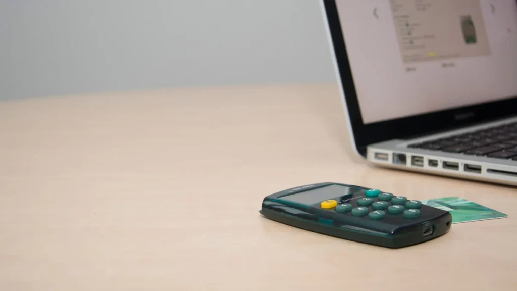 Calculator and credit card beside a laptop on a desk.