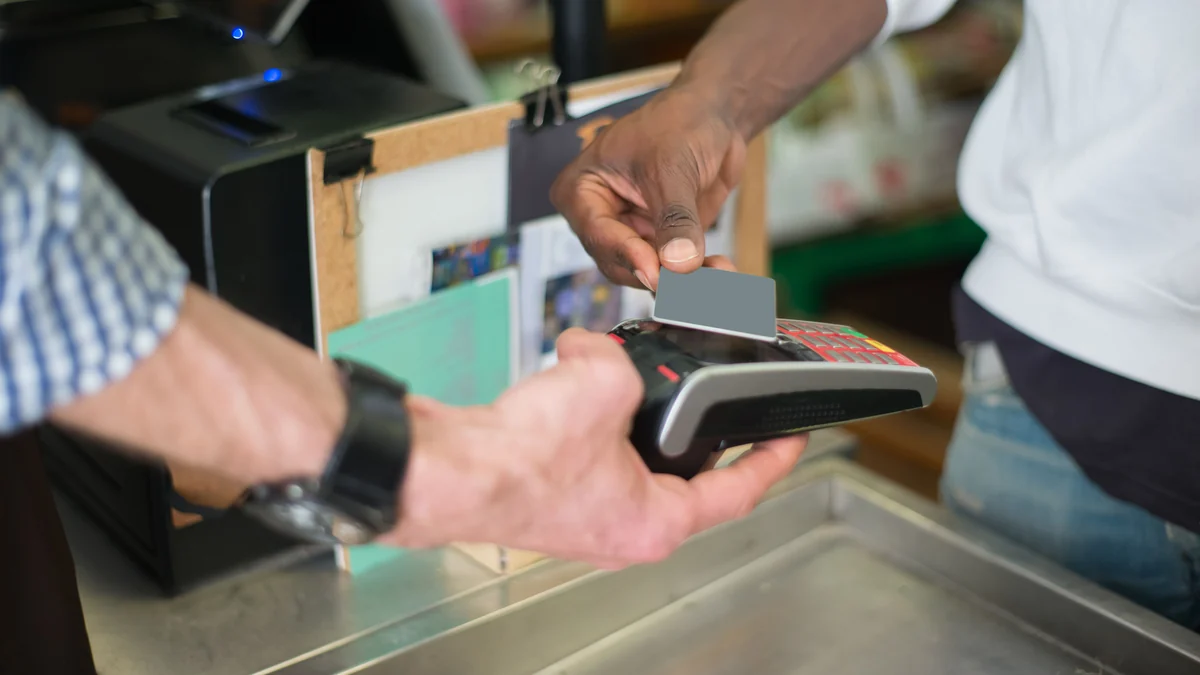A customer tapping a payment card on a handheld card terminal at a retail checkout.
