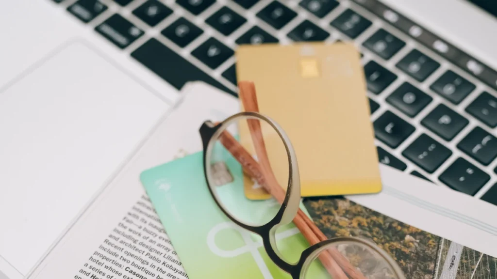 Several credit cards beside eyeglasses on a laptop keyboard and printed reading material.