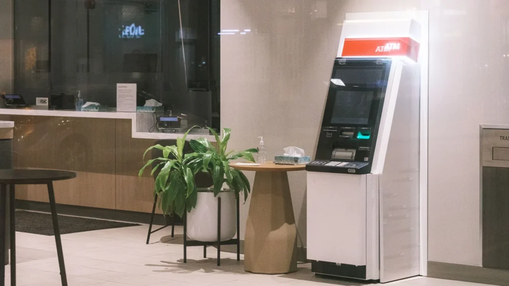 ATM in a modern bank lobby beside a plant and seating area.