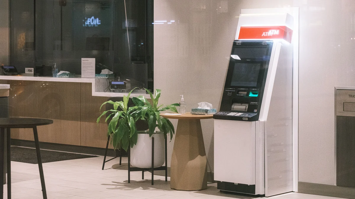ATM in a modern bank lobby beside a plant and seating area.