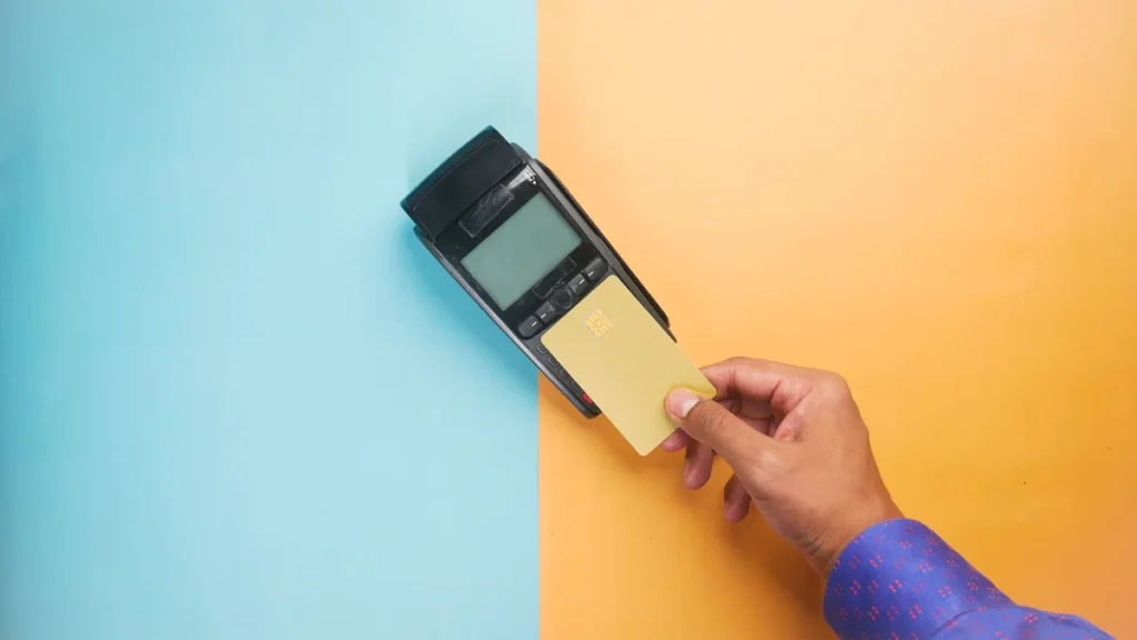 A hand tapping a credit card on a payment terminal.