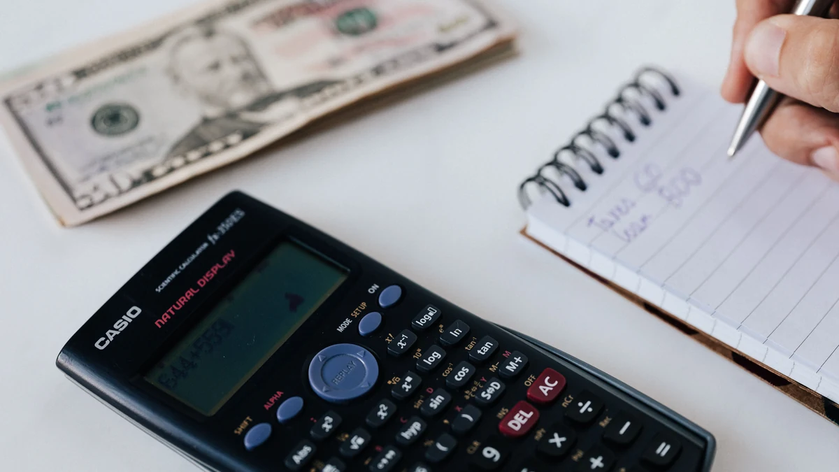 A calculator, cash and a hand writing figures in a notebook.