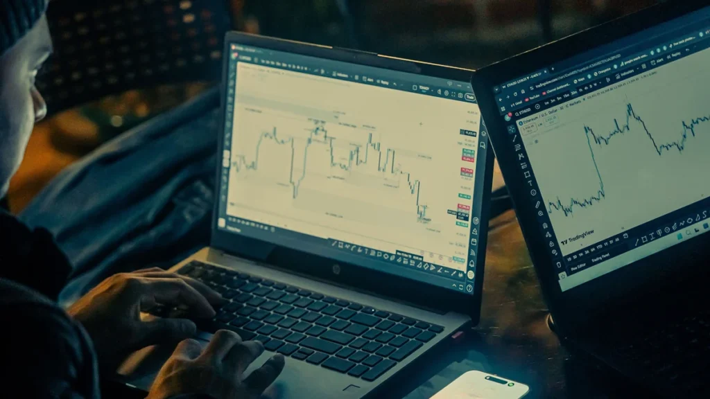 A person analyzing stock-market charts on two laptop screens at night.