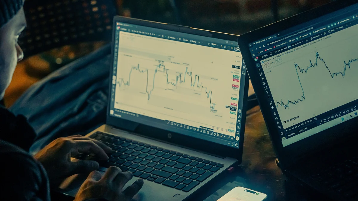 A person analyzing stock-market charts on two laptop screens at night.