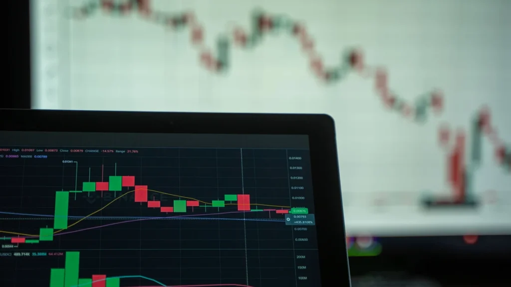 Candlestick stock charts and moving-average lines displayed on two digital screens.