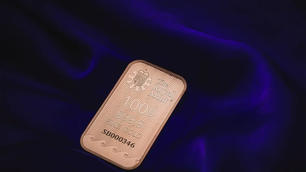 A 100-gram fine gold bar resting on dark purple fabric.