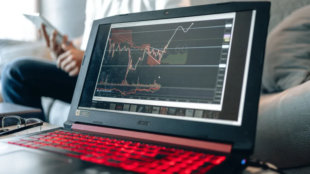 Laptop displaying stock market charts while an investor reviews information nearby.