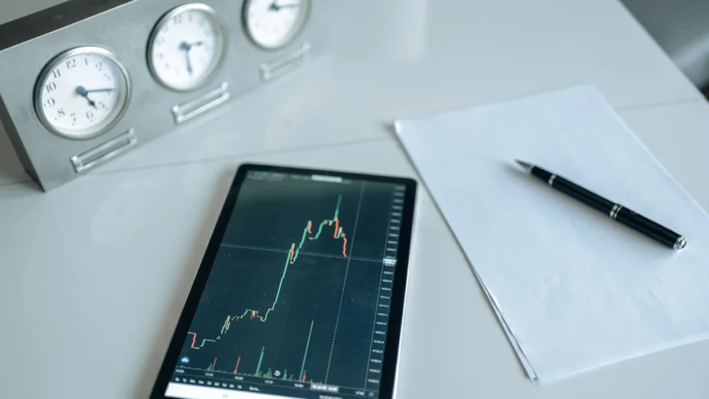 A tablet showing a stock market chart beside several clocks on a trading desk.
