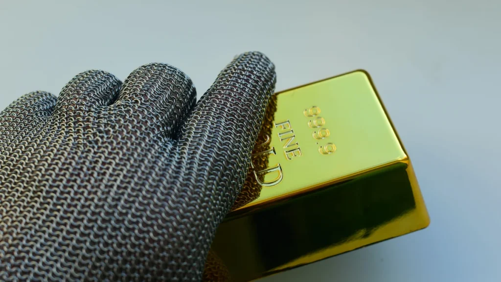 A protective metal glove holding a gold bullion bar.