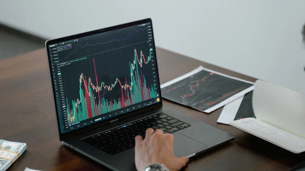 A person reviewing financial market charts on a laptop at a desk.