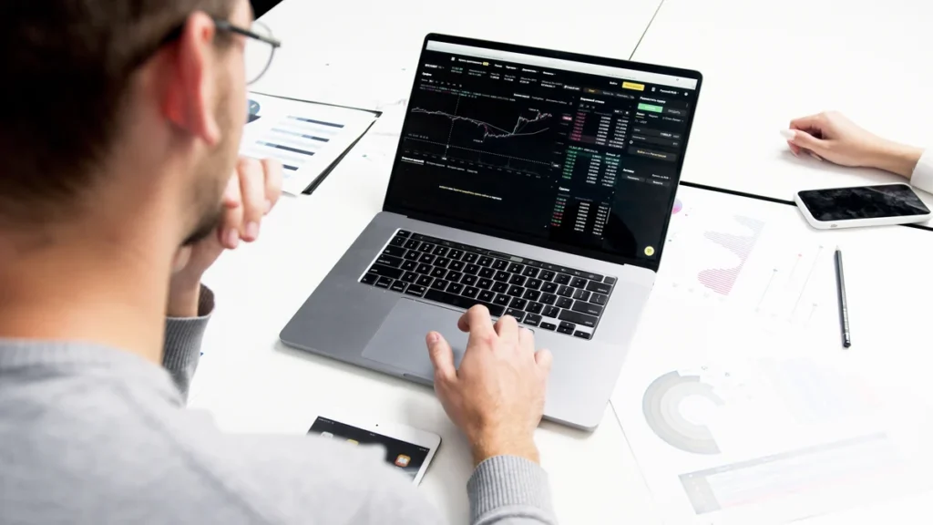 A person using a laptop displaying financial market charts at a desk.