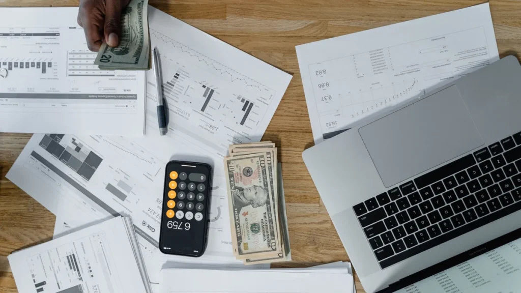 Overhead view of a desk with financial charts, a laptop, a calculator and U.S. dollar bills.