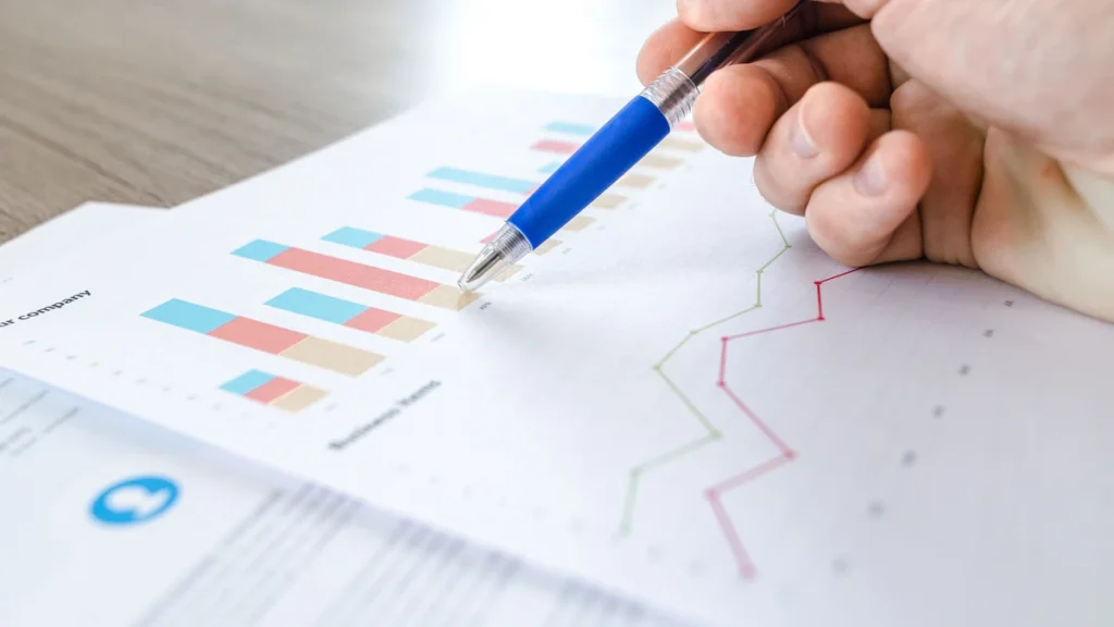 A hand holding a pen over printed financial charts and graphs.