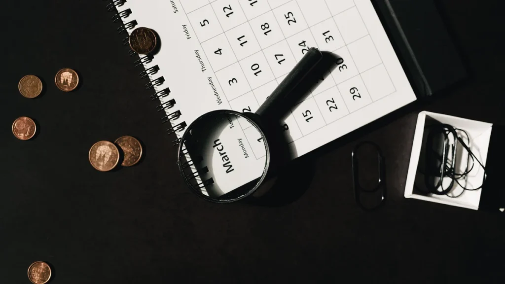 Calendar, magnifying glass and coins on a desk representing investment time horizons.