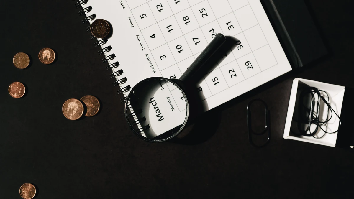 Calendar, magnifying glass and coins on a desk representing investment time horizons.