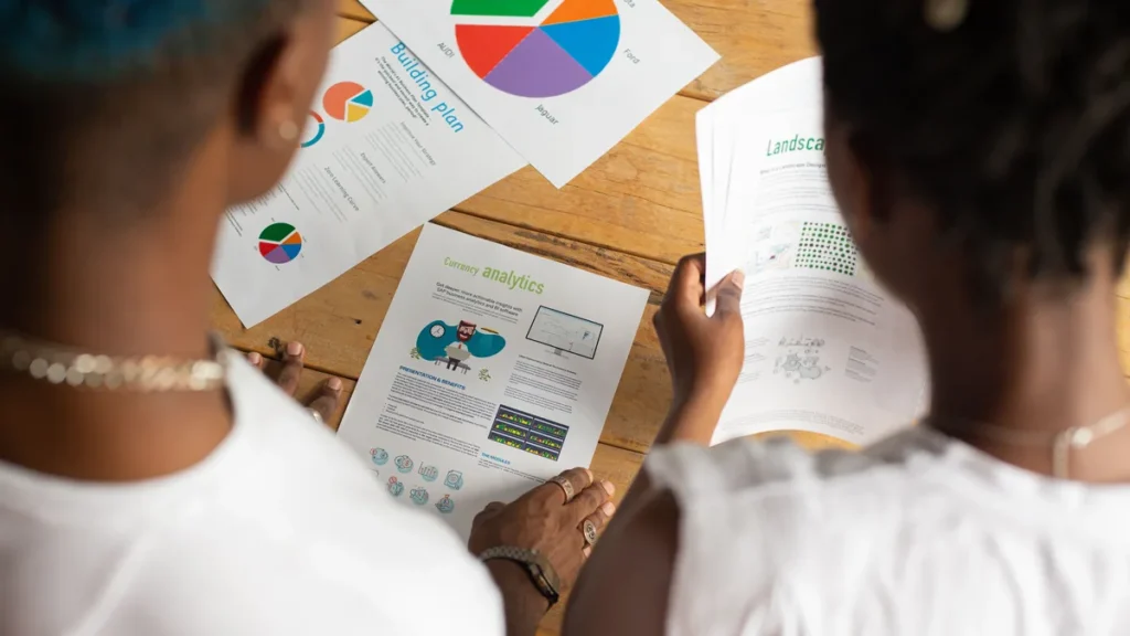 Two people reviewing printed charts and planning documents at a wooden table.