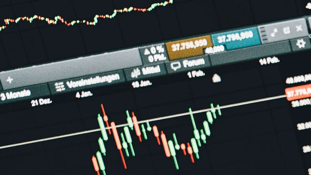 Laptop showing market charts beside a calculator and euro banknotes.