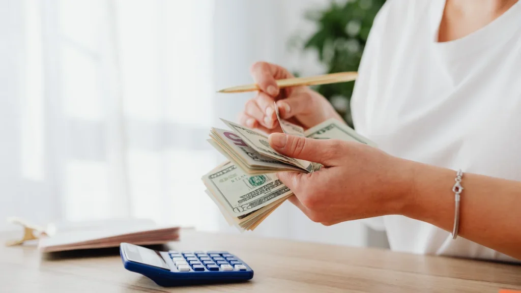 Person counting cash beside a calculator on a desk.