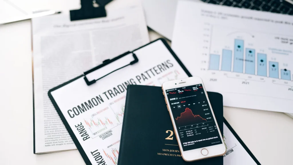 Financial charts, printed reports and a smartphone displaying market data on a desk.
