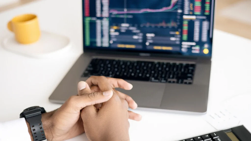 Person seated at a desk with a laptop displaying financial trading charts and a calculator nearby.