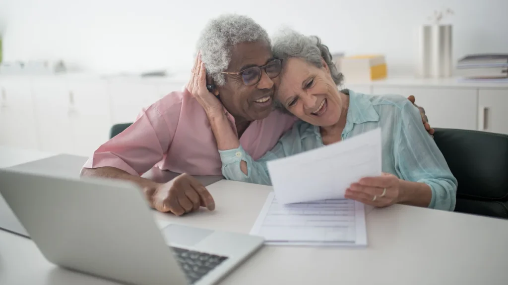 Older couple reviewing financial documents beside a laptop.