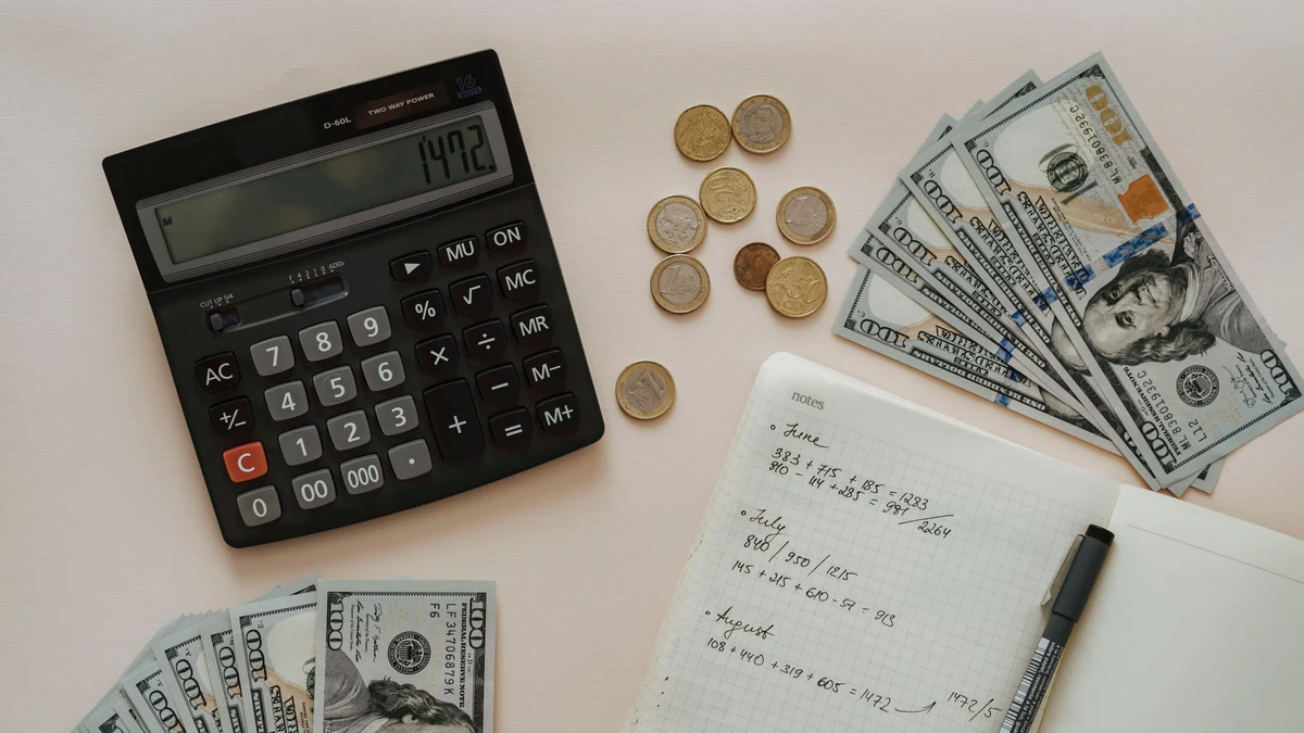 Calculator, cash, coins and a notebook with handwritten budget calculations on a desk.