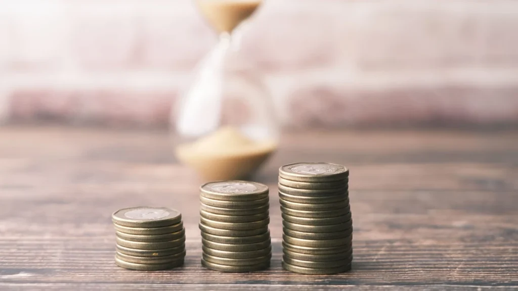 Stacks of coins arranged beside an hourglass on a wooden surface.