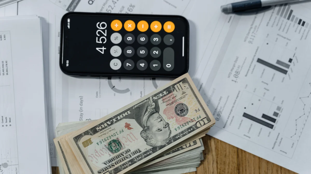 U.S. dollar bills, a calculator app and financial reports arranged on a desk.
