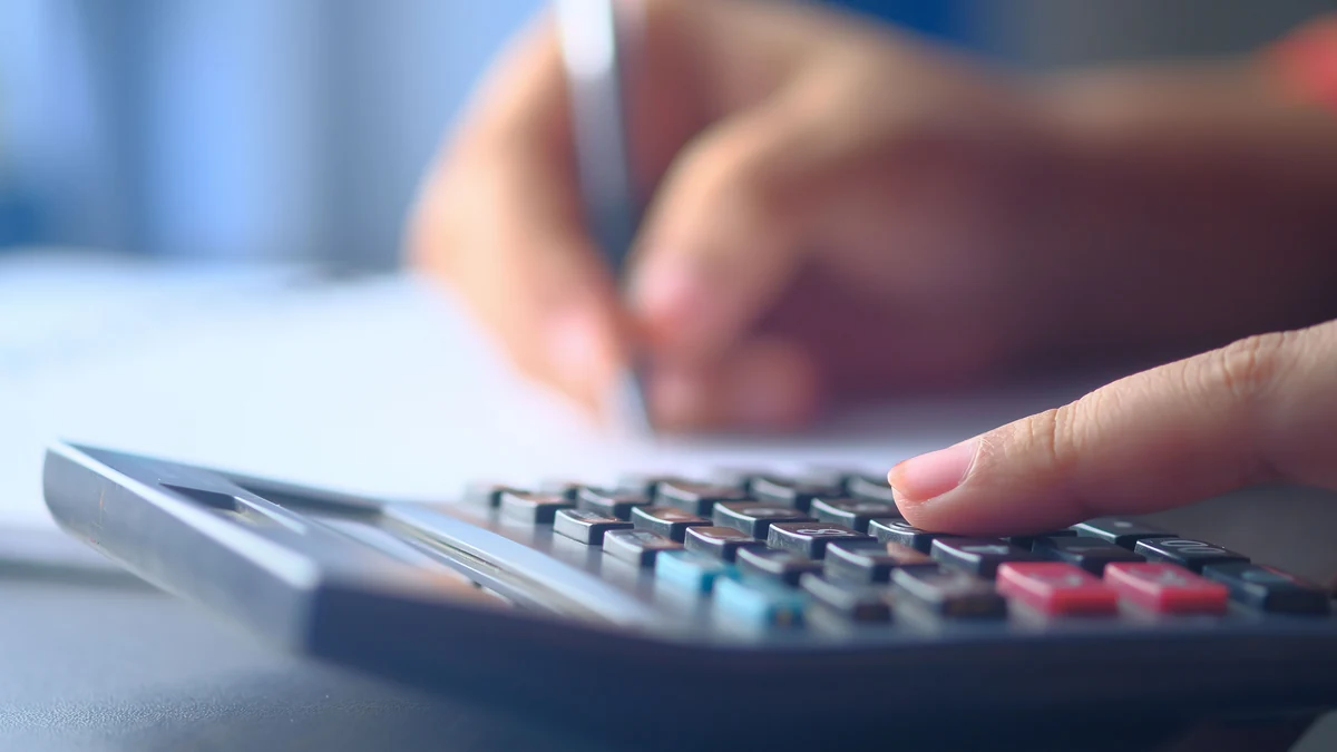 Close-up of hands using a calculator while writing notes.