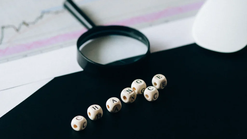 Magnifying glass beside letter beads spelling chance on financial charts.