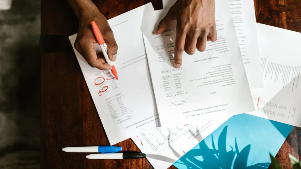 Hands reviewing financial documents with a marker on a desk.