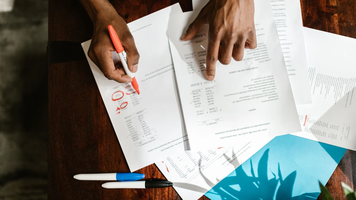 Hands reviewing financial documents with a marker on a desk.