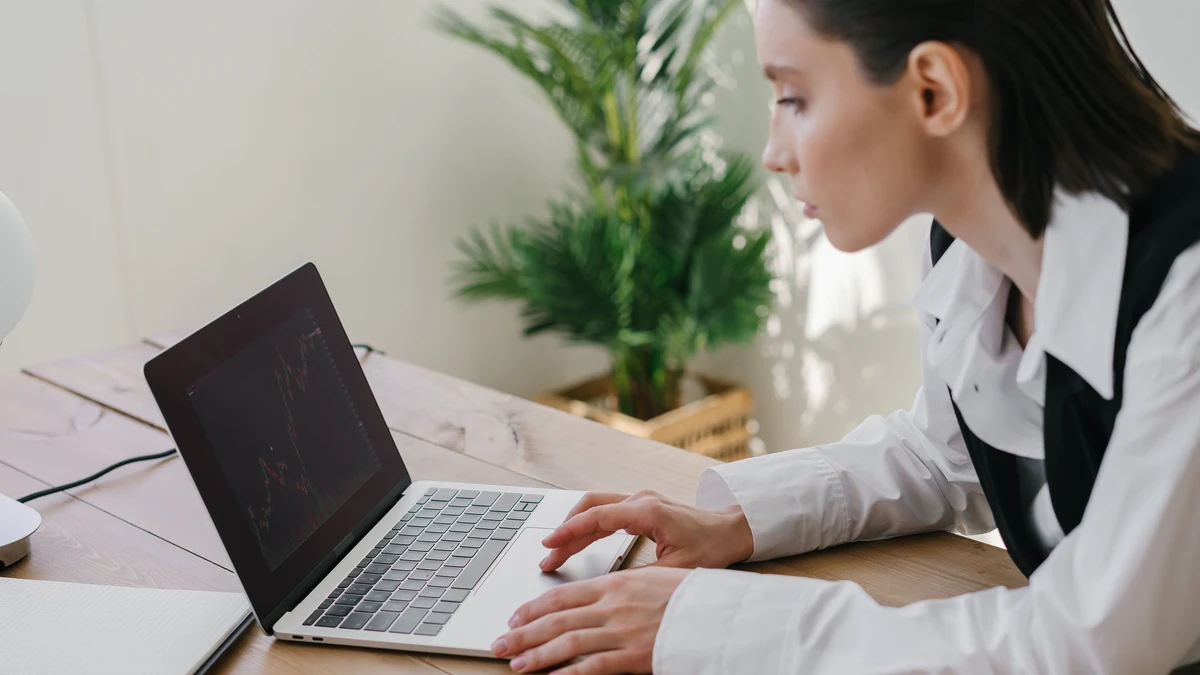 A professional reviewing financial market charts on a laptop at a desk.