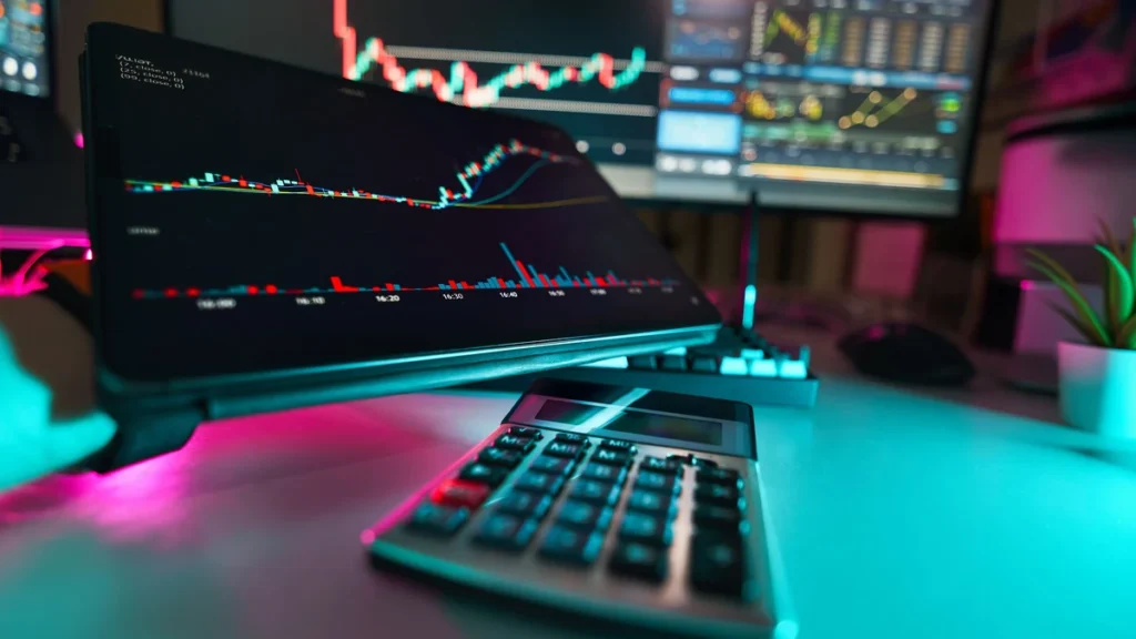Financial market charts displayed on several screens beside a calculator.