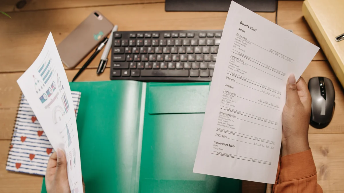 Hands reviewing financial statements and charts at a desk.
