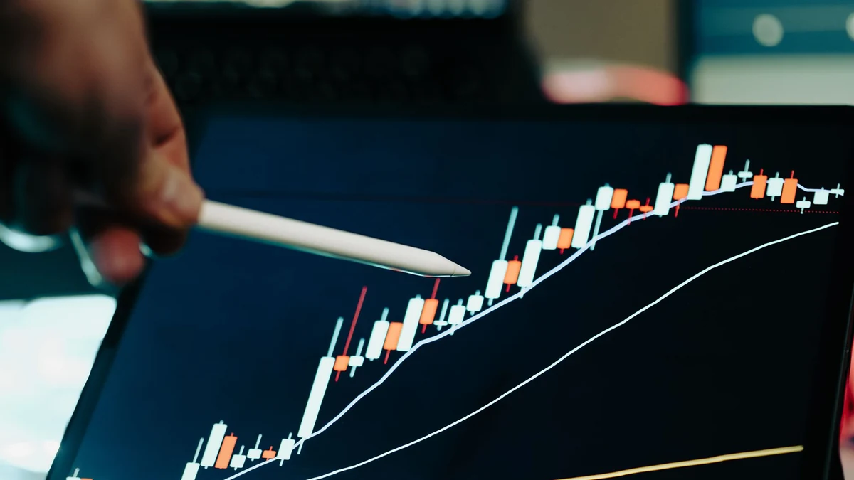 Digital tablet displaying a financial market candlestick chart with blurred trading screens in the background.