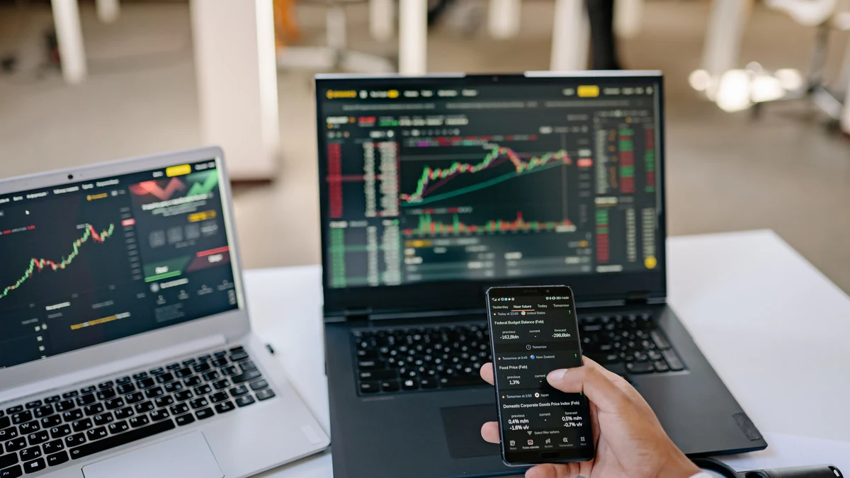 Trading charts displayed on two laptops beside a smartphone.