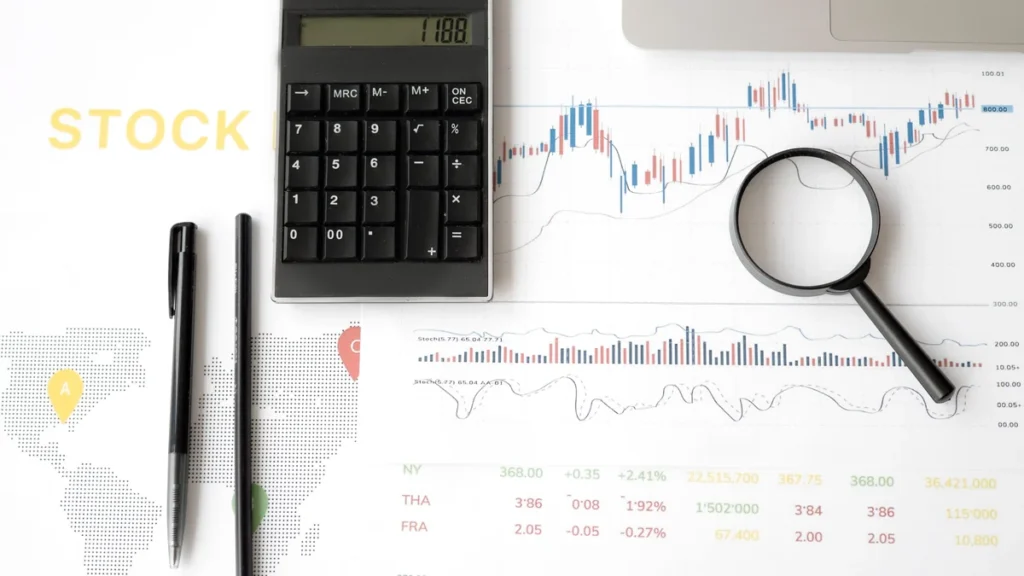 A calculator and magnifying glass on financial market charts.