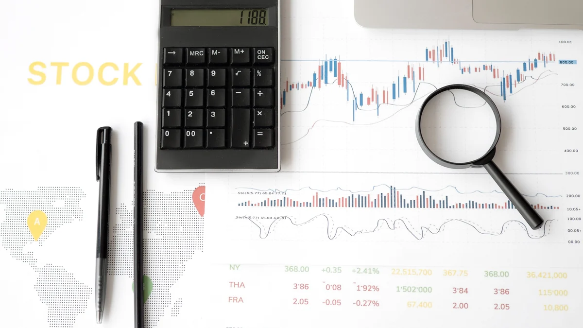 A calculator and magnifying glass on financial market charts.