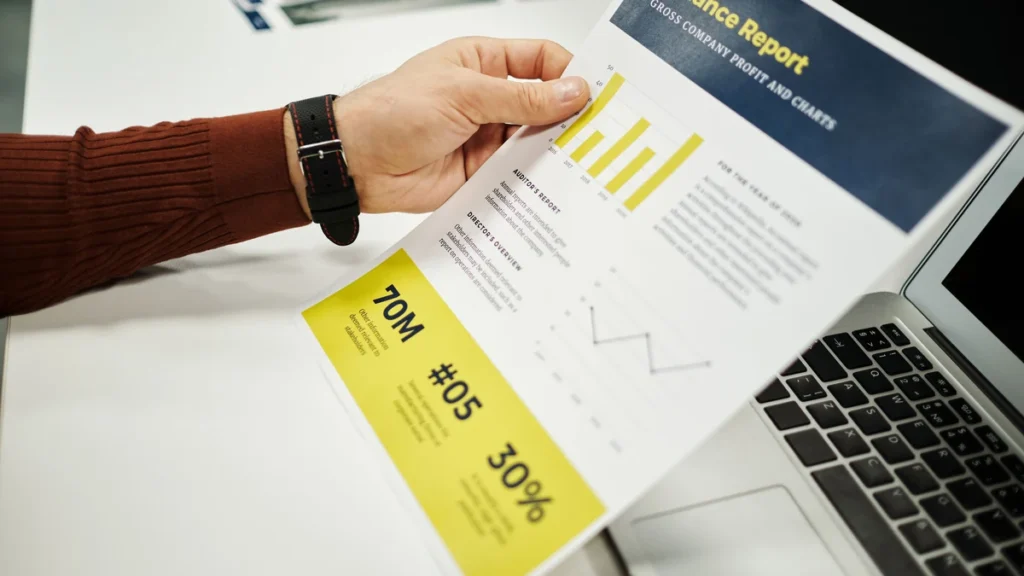 A person reviewing a finance report with charts beside a laptop.