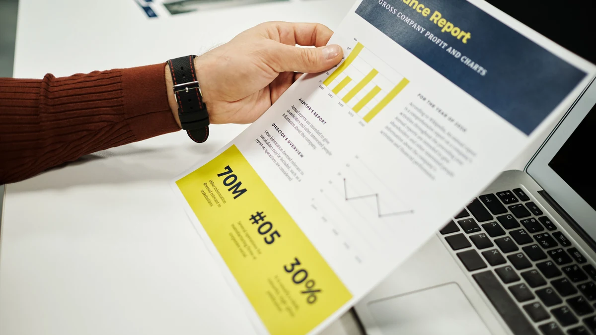A person reviewing a finance report with charts beside a laptop.