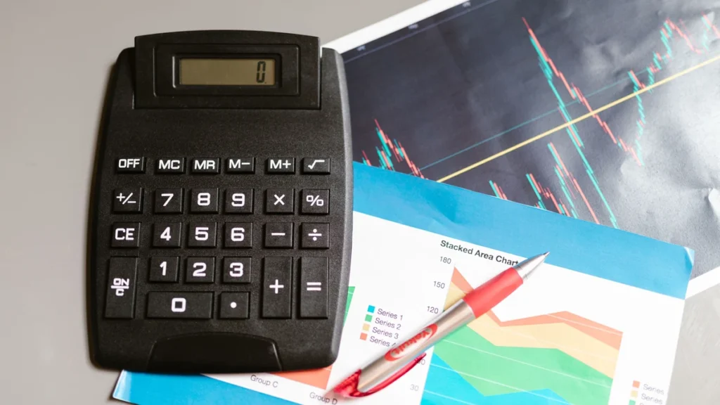 Calculator beside printed financial charts and graphs on a desk.