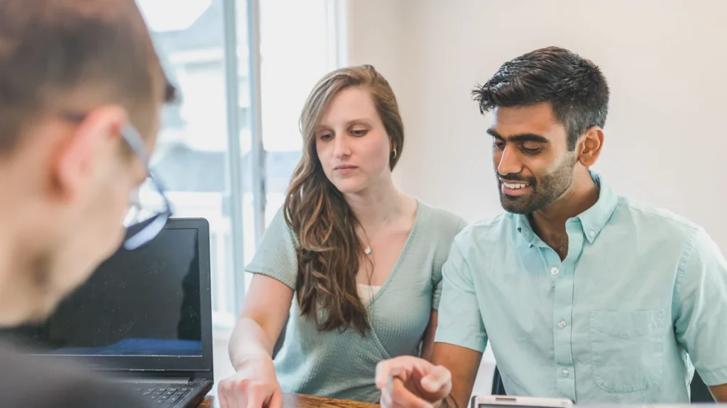 A financial adviser meeting with a couple at a desk with a laptop and calculator.