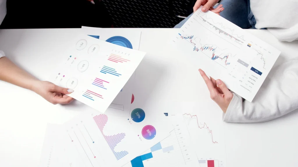 Hands holding printed financial charts over a table covered with investment graphs.