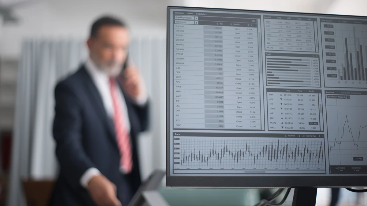 Financial market data displayed on a computer monitor with a business professional in the background.